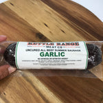 A hand holding a vacuum-sealed package of Garlic Uncured All Beef Summer Sausage from Redneck Range, placed on a wooden surface.
