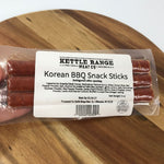 A package of Kettle Range Korean BBQ Snack Sticks in a clear plastic bag with a white label, resting on a wooden surface.