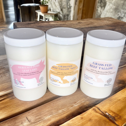 Three plastic containers of animal fat by The Fat Lady: pork leaf lard and two types of grass-fed beef tallow, on a wooden table.