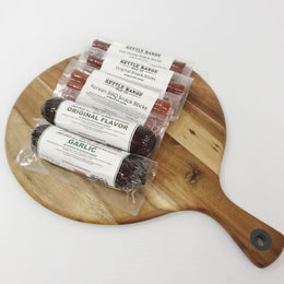 Three Kettle Range Korean BBQ snack sticks, including Original Flavor and Garlic, arranged on a round wooden serving board against a white background.