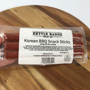 A package of Kettle Range Korean BBQ Snack Sticks in a clear plastic bag with a white label, resting on a wooden surface.