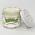 A jar of catnip and neem tallow bug repellent with its lid leaning against it on a clean white background. The product is in a clear glass jar showing the off-white cream inside, with a white label featuring green and black text.